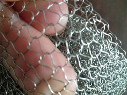 A hand is holding a piece of knitted wire mesh with round wires.